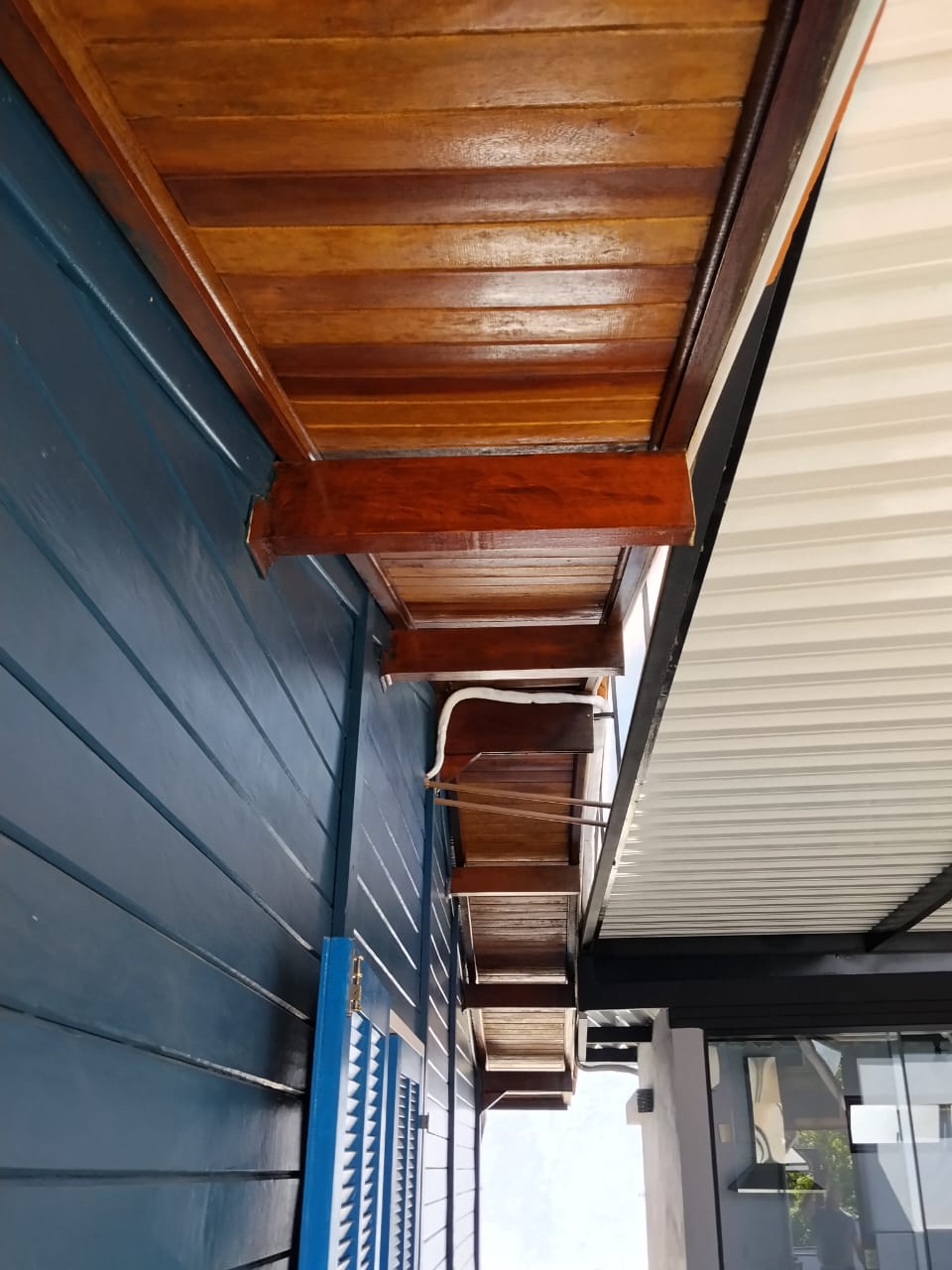Forro de madeira maciça em varanda de residência com fachada azul