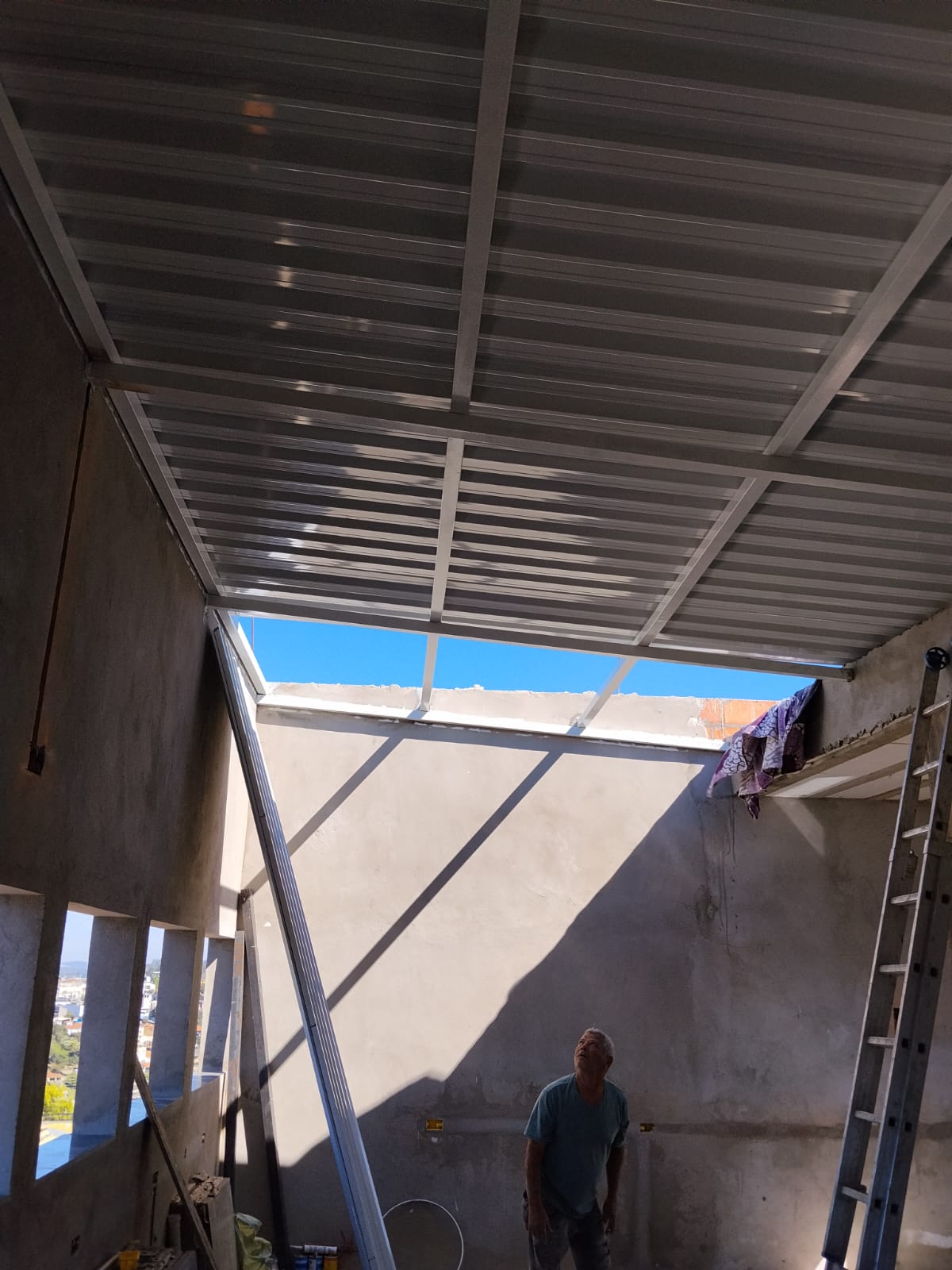 Vista interna da cobertura metálica com estrutura pintada de branco em laje residencial